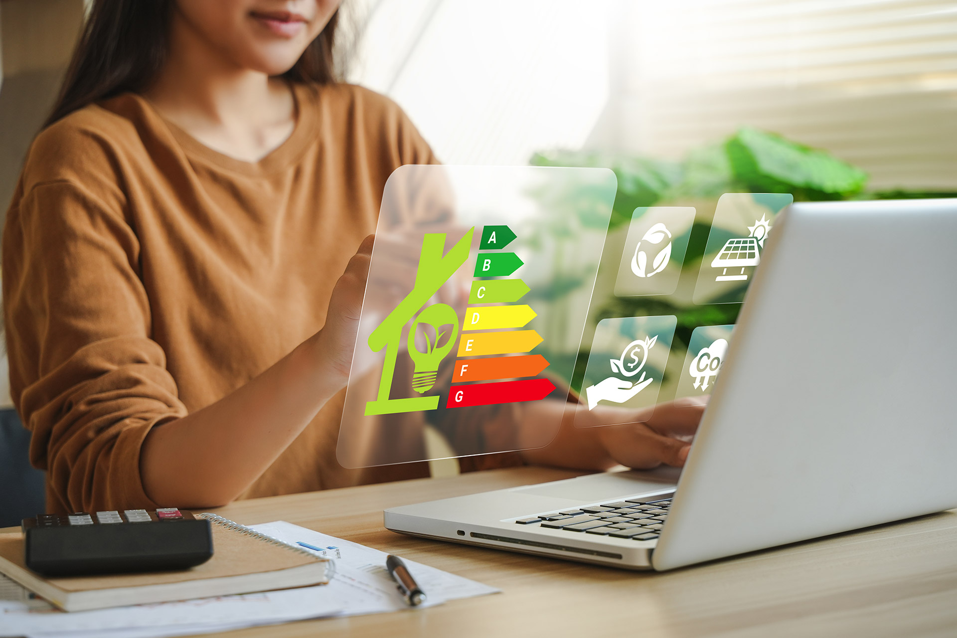 Frau am Laptop mit holografischer Energieeffizienz-Anzeige und grünen Nachhaltigkeitssymbolen