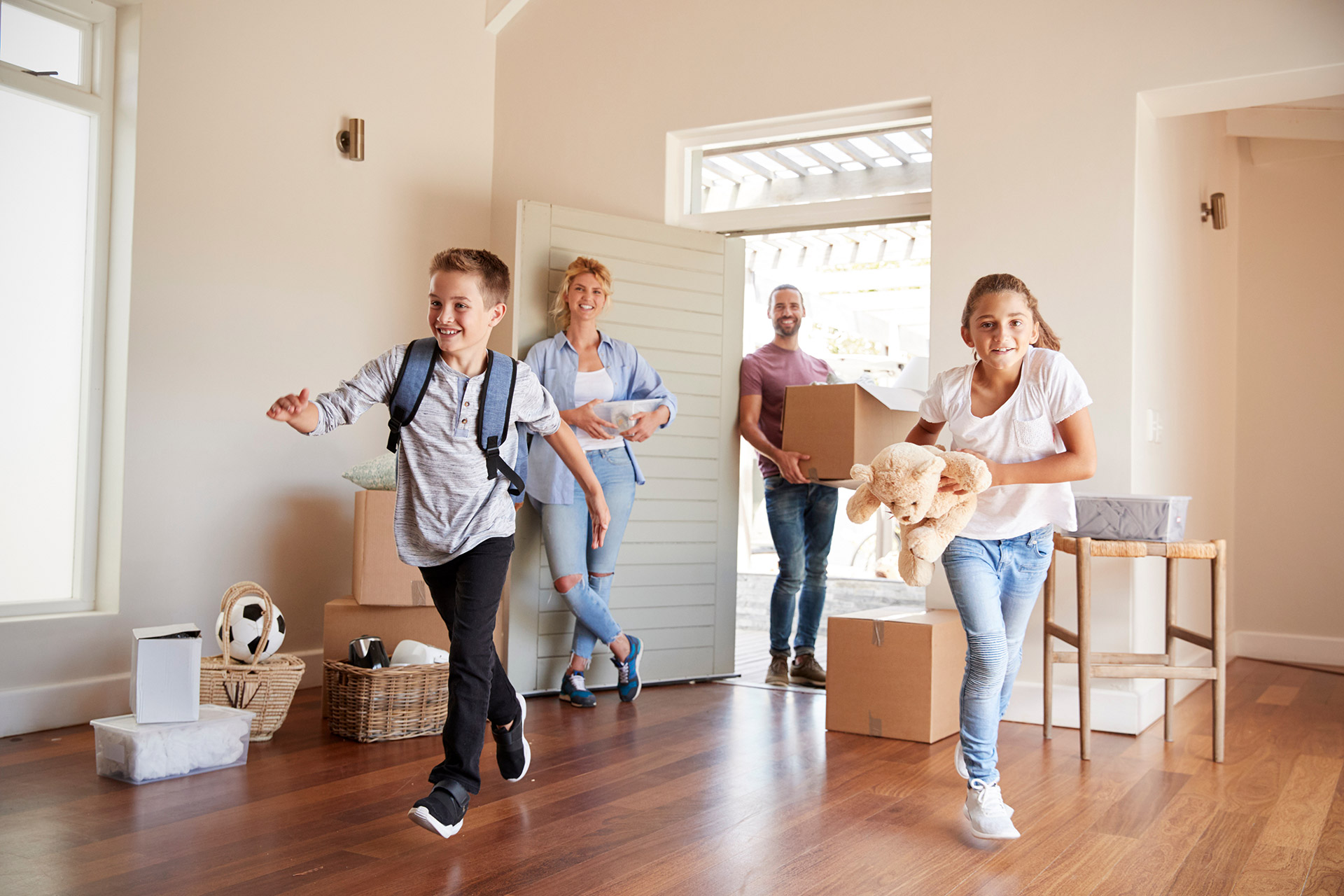 Familie mit Kindern trägt Umzugskartons in neues Zuhause mit hellem Wohnzimmer und Parkettboden